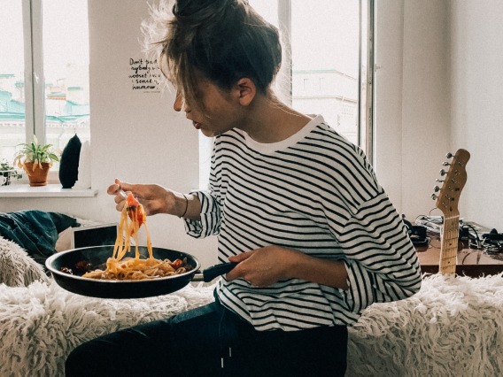 women in striped shirt eating pasta in apartment